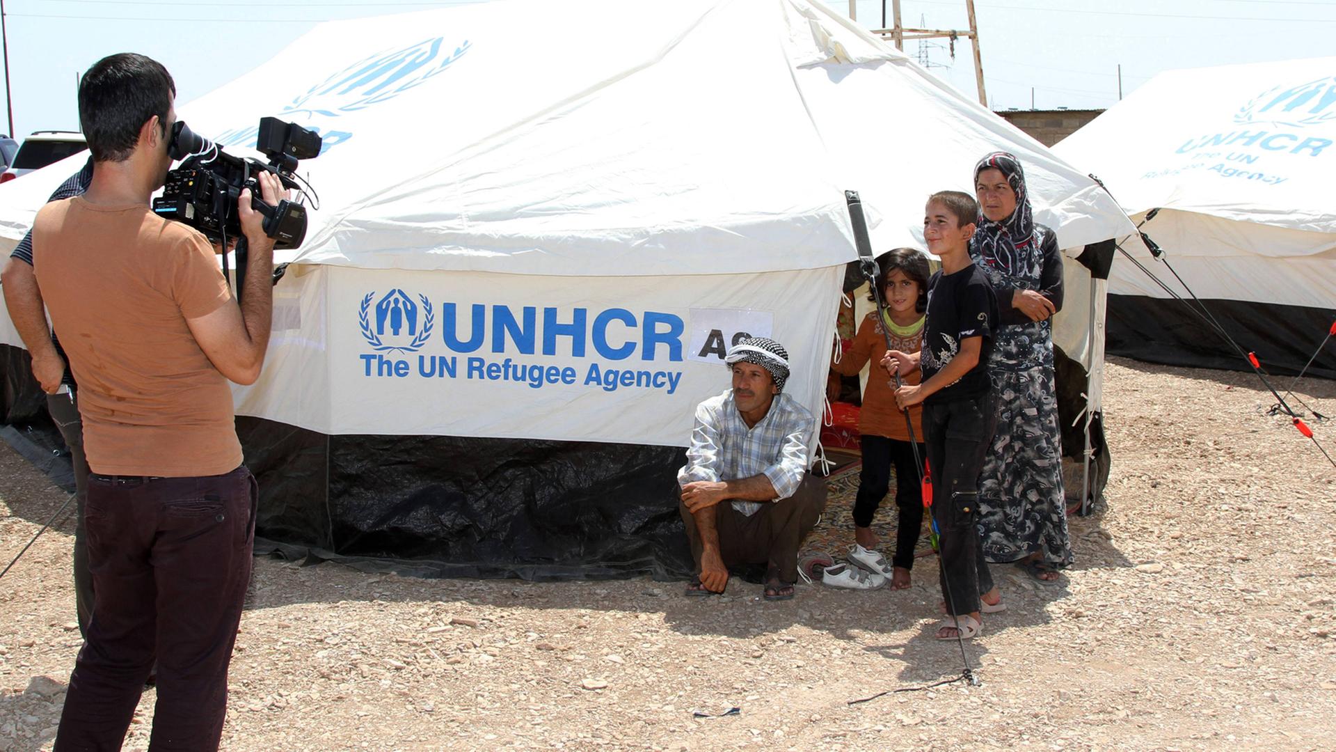 Ein Kameramann filmt eine Flüchtlingsfamilie an einem UNHCR-Zelt