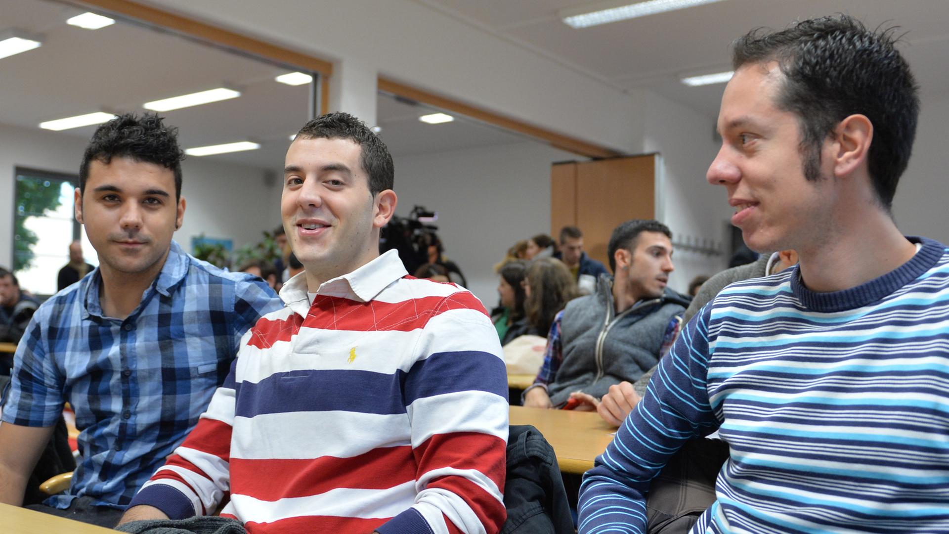 Drei junge Spanier sitzen in einem Konferenzraum an einem Tisch