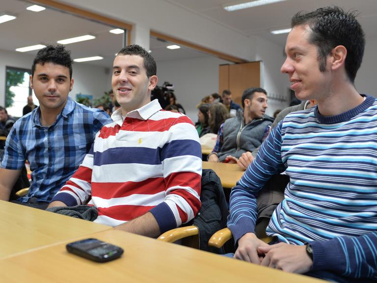 Drei junge Spanier sitzen in einem Konferenzraum an einem Tisch