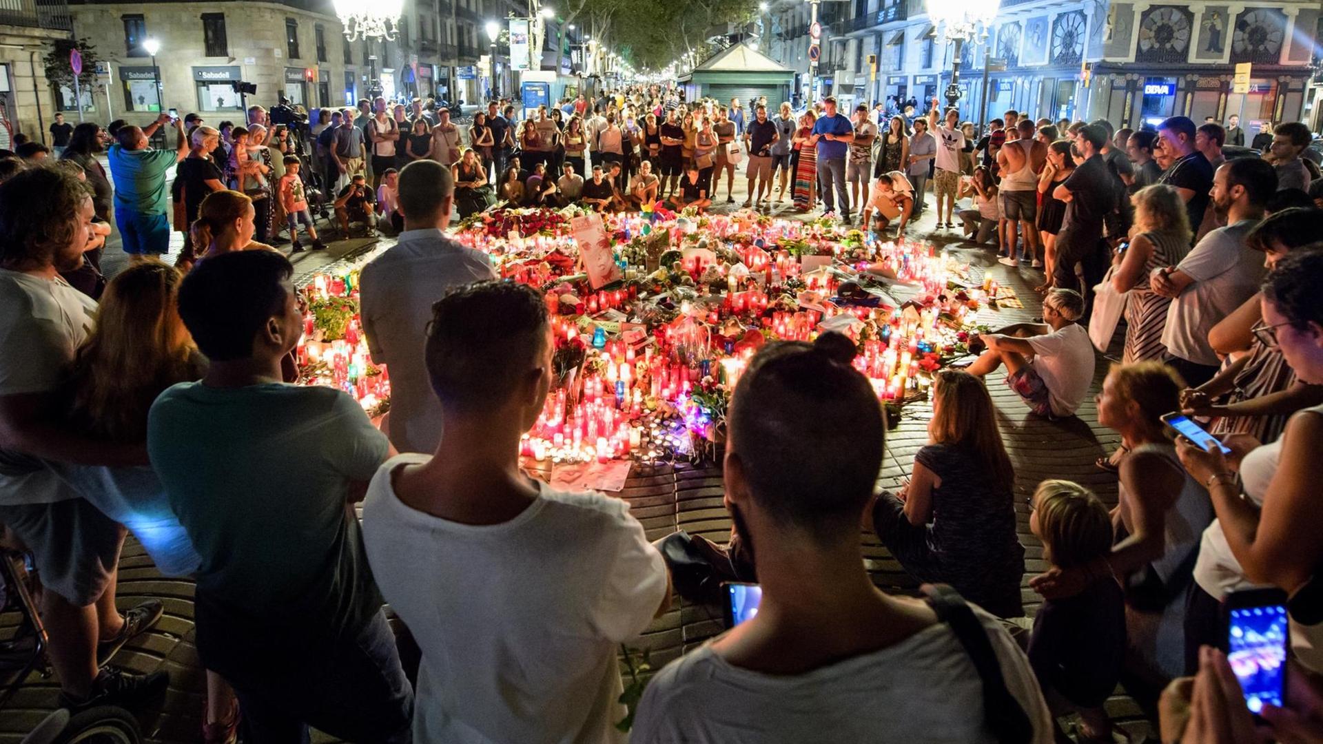 Zahlreiche Menschen stehen am 19.08.2017 auf der Flaniermeile Las Ramblas in Barcelona (Spanien) im Kreis um niedergelegte Blumen und Kerzen. Auf der Straße war am 17.08. ein Lieferwagen in eine Menschenmenge gefahren. Bei dem Terroranschlag auf der Promenade wurden mindestens 13 Menschen getötet und zahlreiche verletzt. (zu dpa "Kerzen, Blumen und Stofftiere - Barcelona gedenkt der Terroropfer" vom 19.08.2017) Foto: Matthias Balk/dpa +++(c) dpa - Bildfunk+++