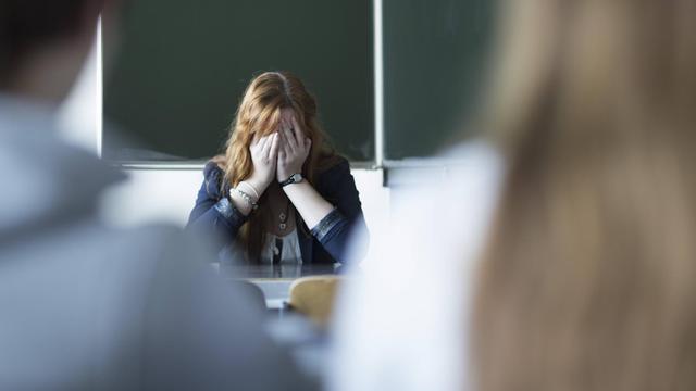 Das gestellte Foto zeigt eine verzweifelte Lehrerin im Klassen-Zimmer.
