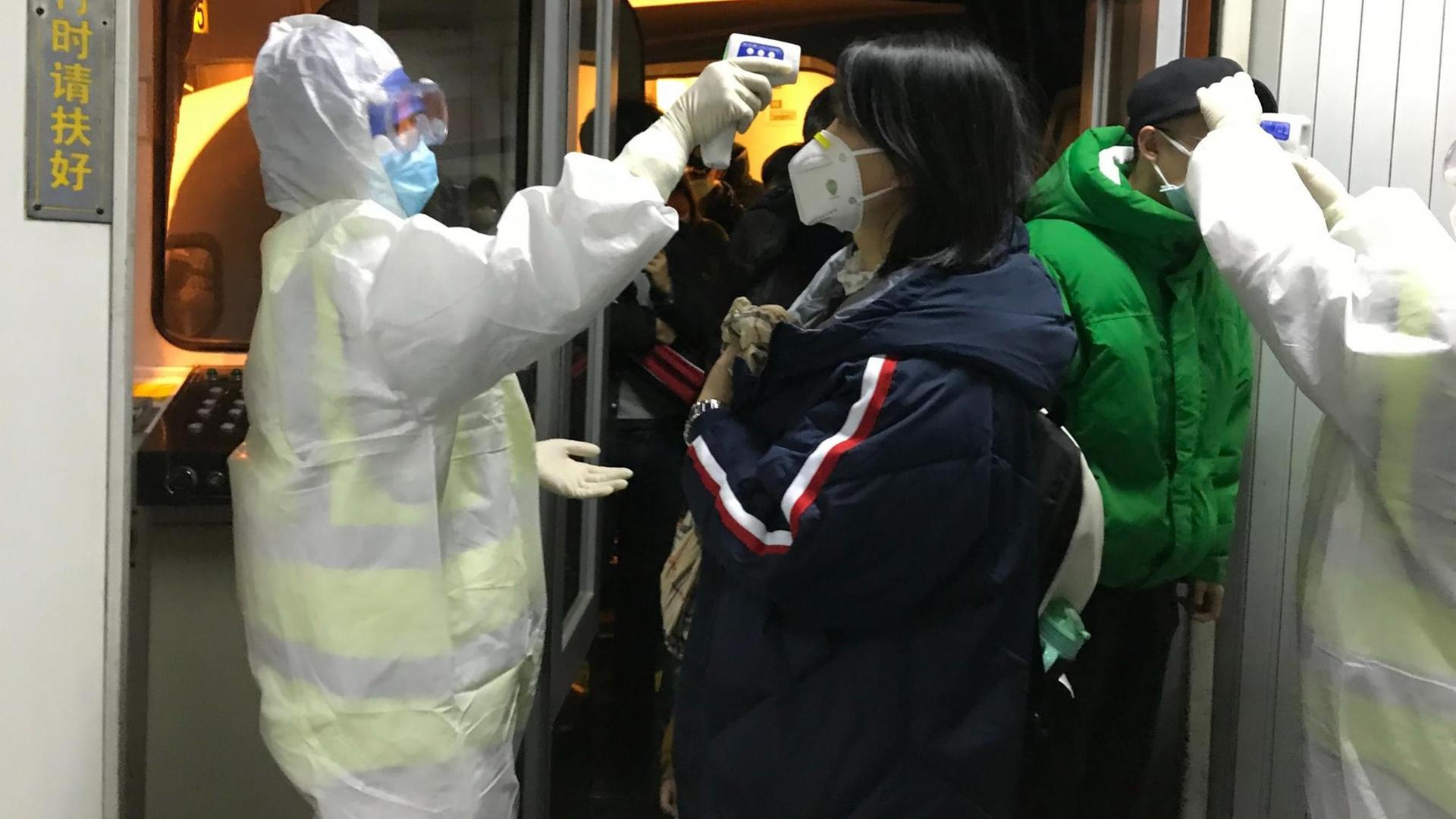 Das Bild zeigt chinesische Gesundheitsbeamte in Schutzanzügen. Sie kontrollieren am Flughafen von Peking die Körpertemperatur von Passagieren, die aus der Stadt Wuhan angereist sind.