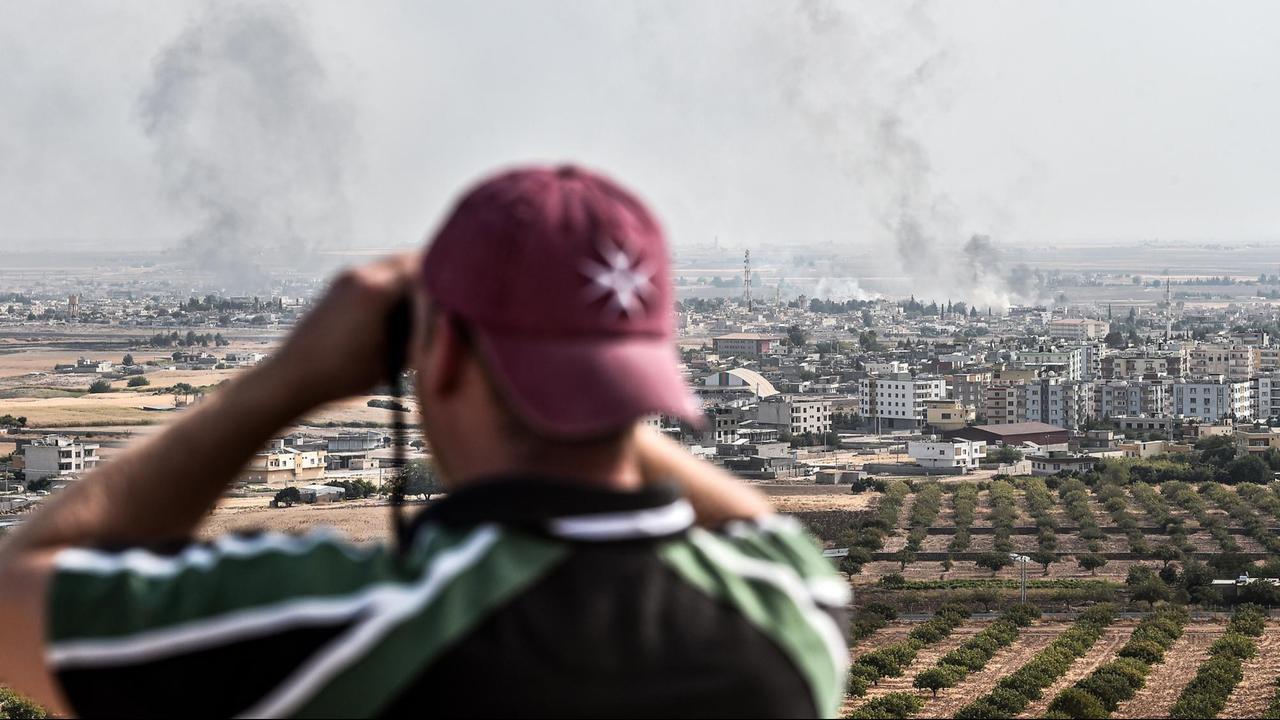Ein Mann schaut an der türkisch-syrischen Grenze durch ein Fernglas auf die syrische Stadt Ras al-Ain, aus der Rauch aufsteigt