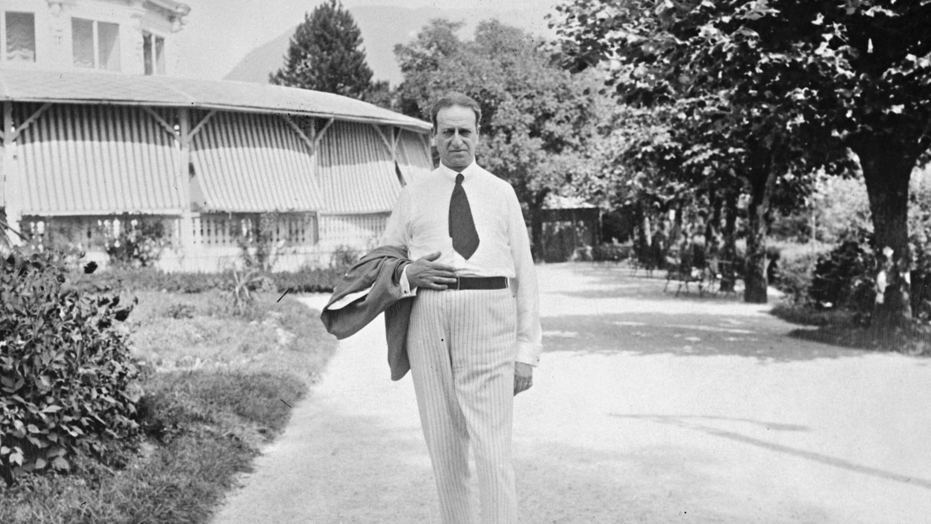 Oscar Straus steht in einem Park vor einer großen Villa.