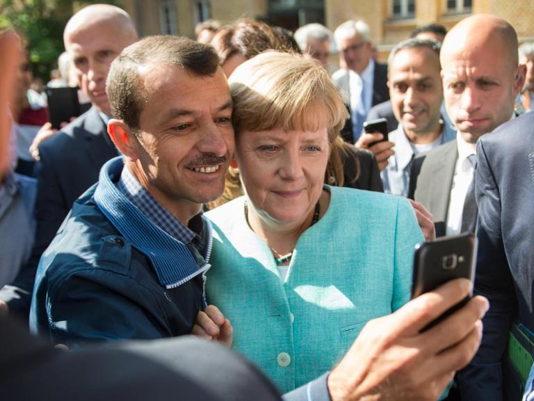 Bundeskanzlerin Angela Merkel (CDU) lässt sich am 10.09.2015 nach dem Besuch einer Erstaufnahmeeinrichtung für Asylbewerber der Arbeiterwohlfahrt (AWO) und der Außenstelle des Bundesamtes für Migration und Flüchtlinge in Berlin-Spandau für ein Selfie zusammen mit einem Flüchtling fotografieren. Foto: Bernd von Jutrczenka/dpa