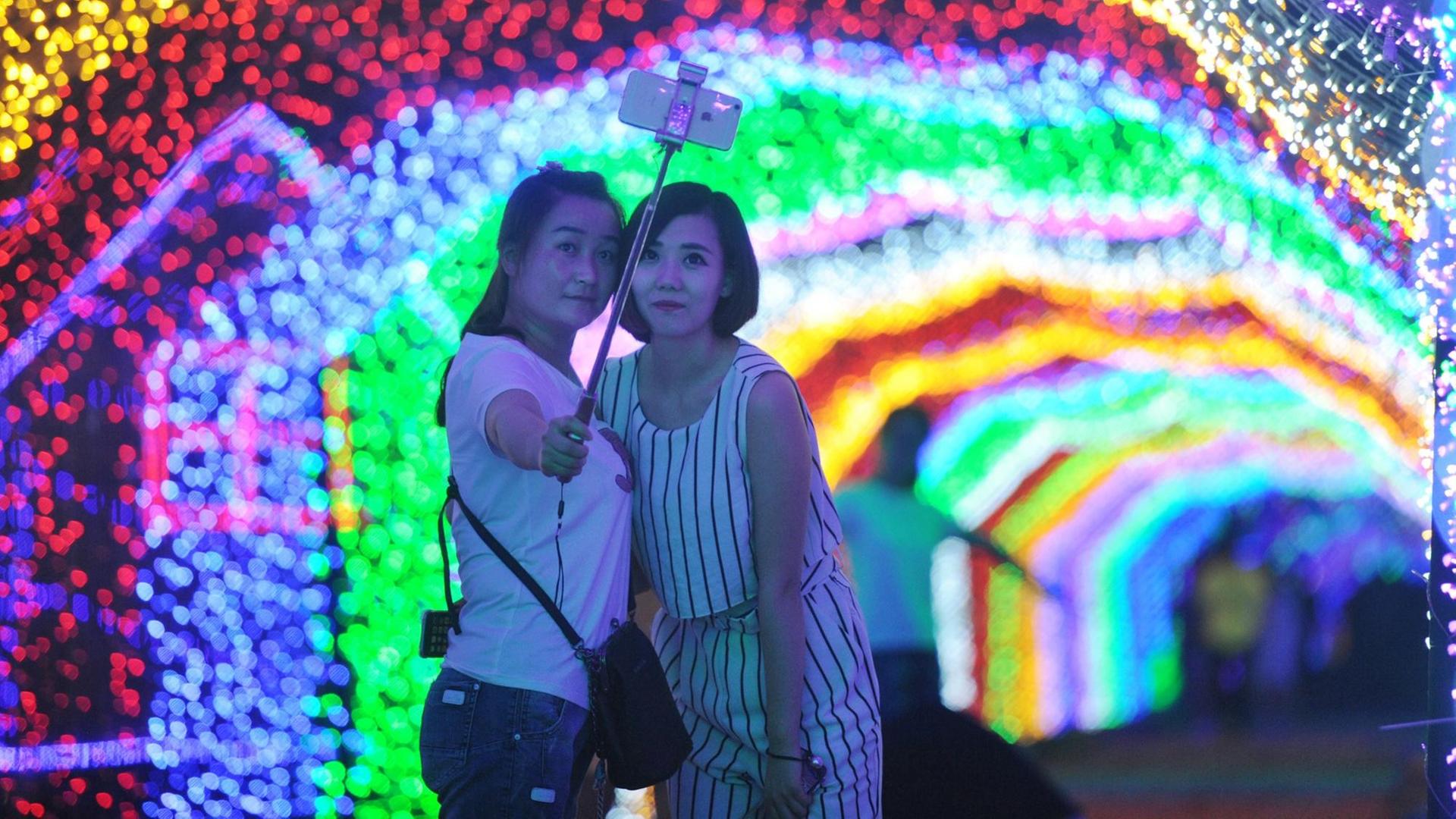 Zwei Frauen fotografieren sich mit einem Selfie-Stick vor einer Lichtinstallation.