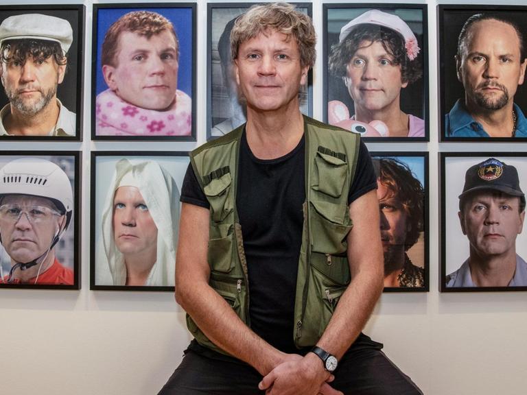Der Künstler Björn Melhus sitzt im Max-Liebermann-Haus vor einer Installation mit Selbstbildnissen.
