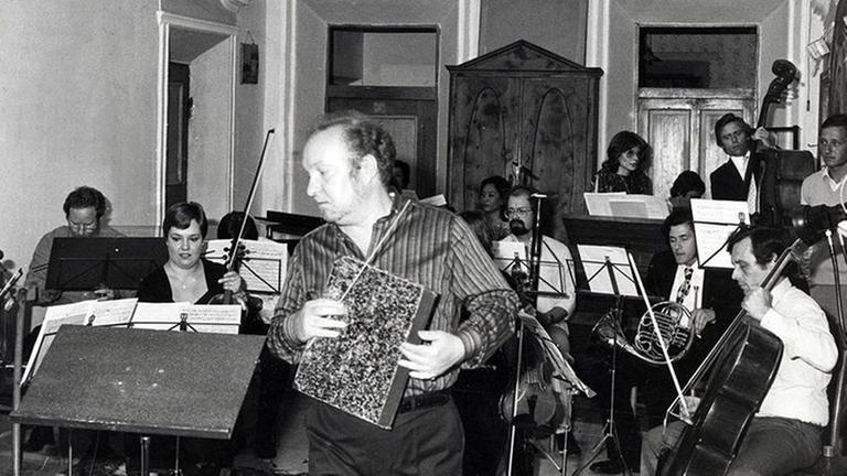 Rainer Riehn mit Noten in der Hand zum Pult gehend, vor dem Ensemble Musica Negativa im Trenkerhof in Toblach