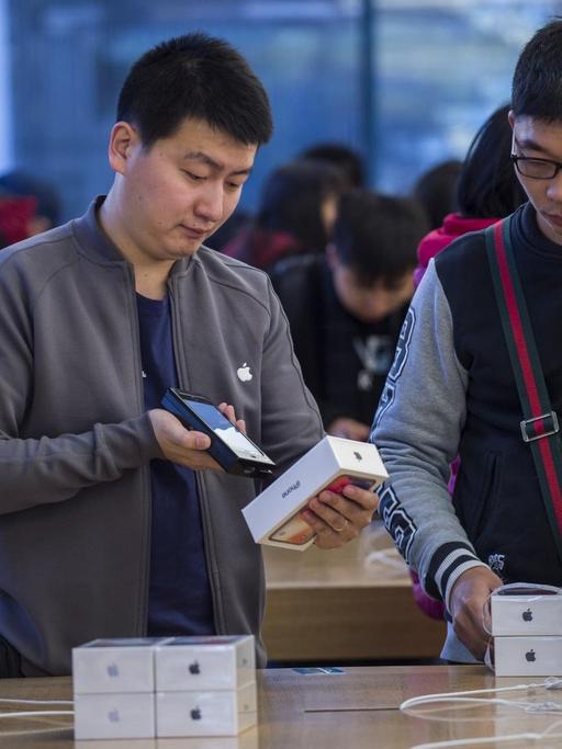 Mehrere Kunden beugen sich in einem Pekinger Geschäft über neue Smartphones von Apple