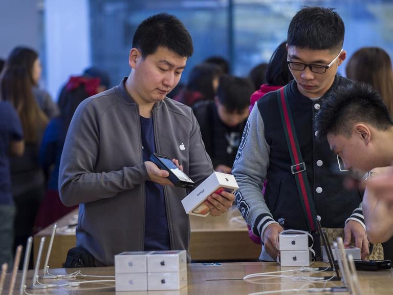 Mehrere Kunden beugen sich in einem Pekinger Geschäft über neue Smartphones von Apple