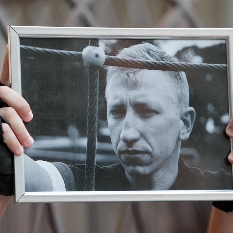 Ein Aktivist in Kiew hält am 3.8.2021 ein Schwarz-Weiß-Porträtfoto des in Kiew tot aufgefundenen belarussischen Aktivisten Vitali Schischow in die Luft.