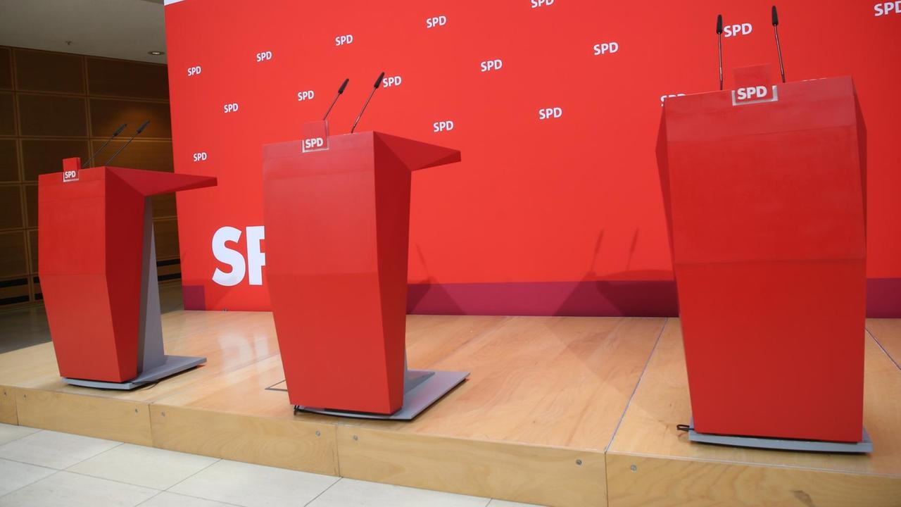 Drei Rednerpulte stehen in der Parteizentrale vor einem roten Hintergrund.