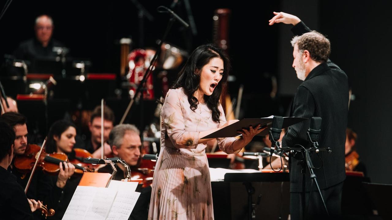 Die Sängerin steht vor dem Orchester neben dem Dirigenten in der Akademie der Künste Berlin.