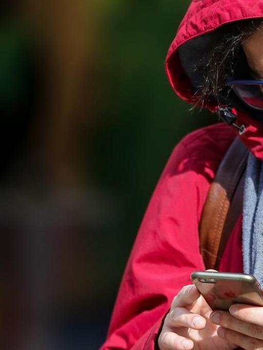 Ein Mann in London mit einer Schutzmaske am 11. März 2020 blickt auf sein Smartphone.