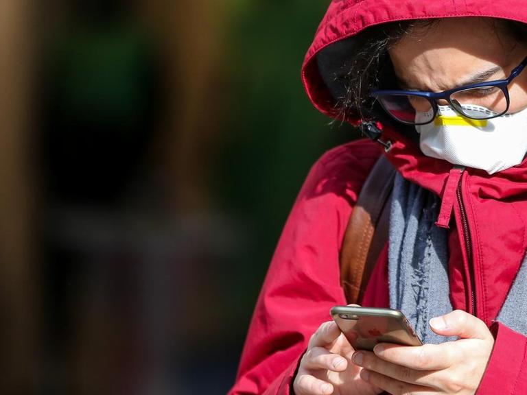 Ein Mann in London mit einer Schutzmaske am 11. März 2020 blickt auf sein Smartphone.