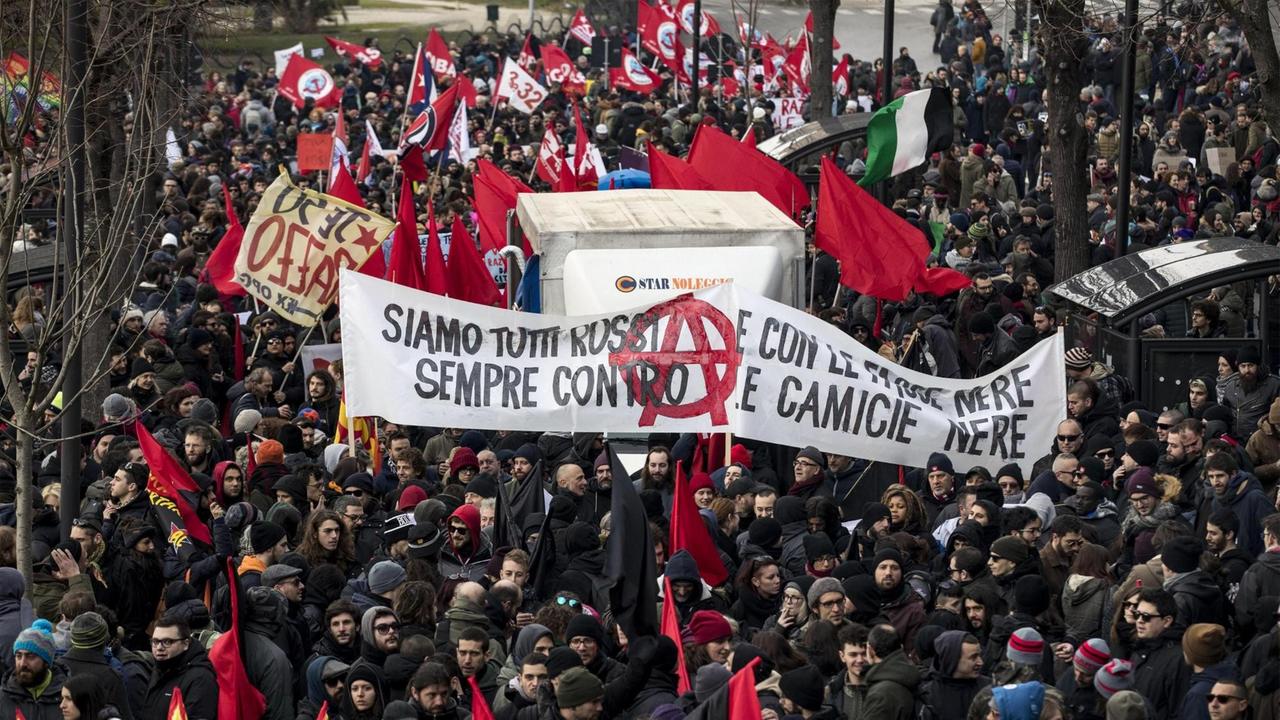 Menschen ziehen in Macerata (Italien) bei einer Demonstration gegen Rassismus durch die Stadt. Sie halten zahlreiche Fahnen und Spruchbänder hoch. 