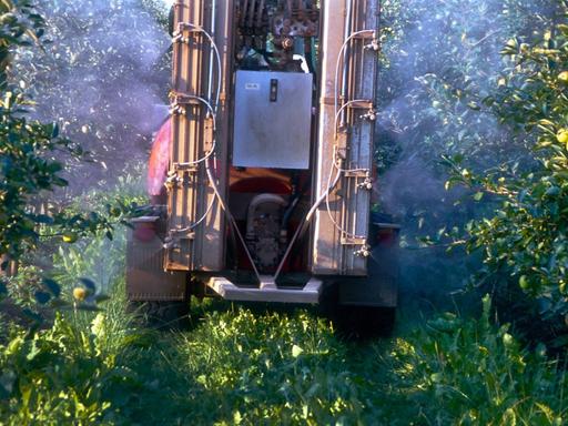 Blick auf einen LKW, von dem aus Apfelbäume mit Pestiziden besprüht werden.