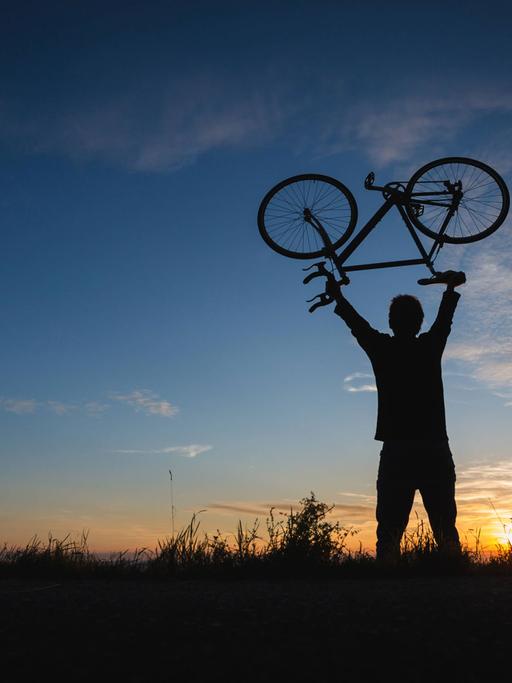 Junger Mann hebt ein leichtes Fahrrad Richtung Himmel