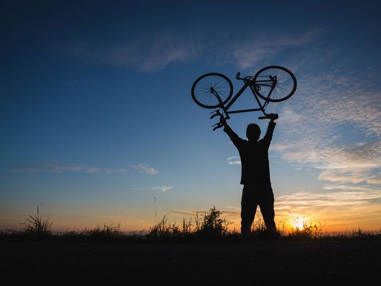 Junger Mann hebt ein leichtes Fahrrad Richtung Himmel