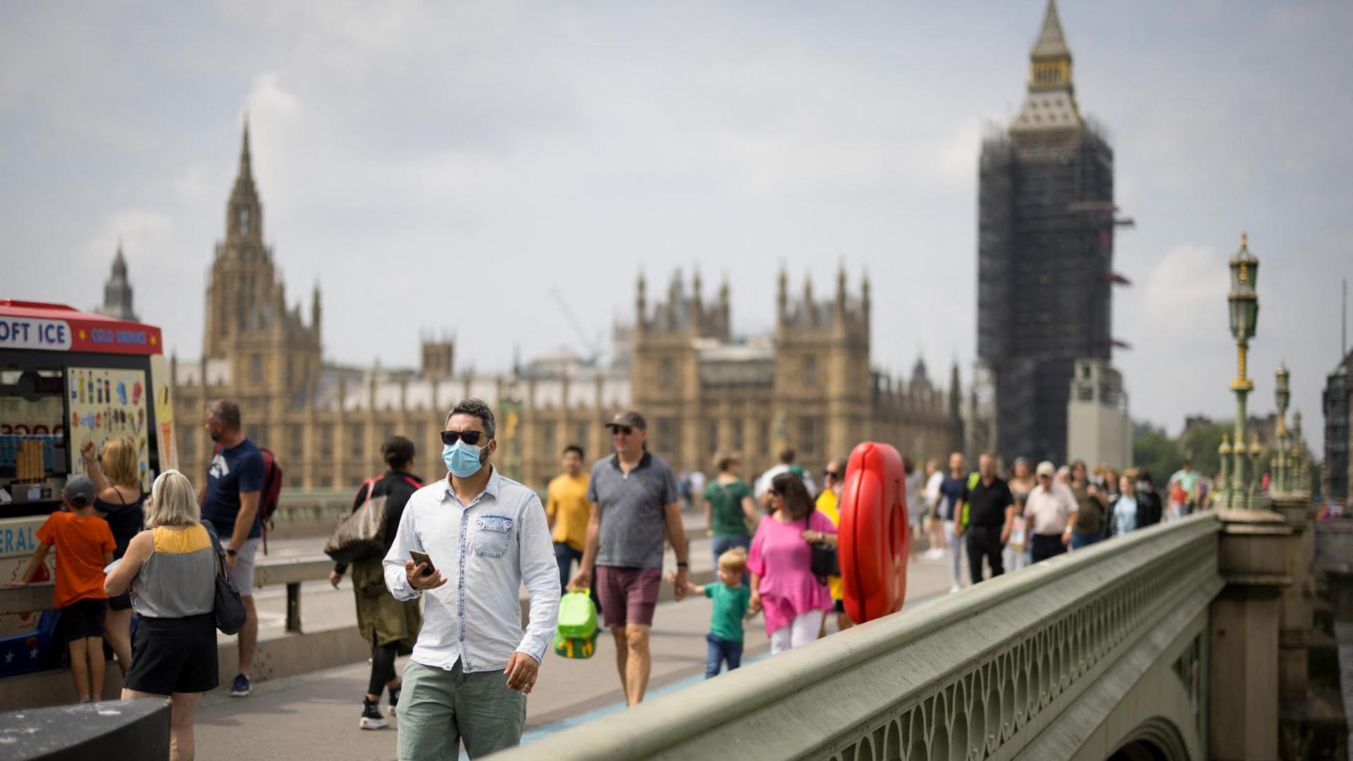 Passanten mit Mund-Nasen-Schutz überqueren die Westminster Bridge in London.