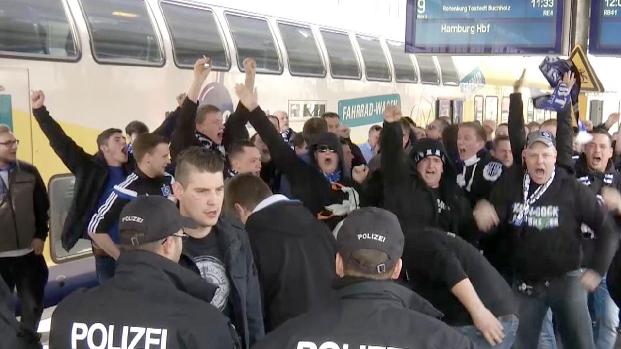 HSV-Fans gehen auf einem Bahnsteig in Bremen Richtung Ausgang des Bahnhofs, nachdem sie mit dem Zug aus Hamburg ankamen und werden dabei von Polizisten beobachtet.