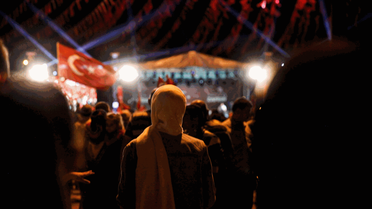 Hazal gerät mitten in den Putschversuch in der Türkei im Jahr 2016. Zu sehen: Demonstration in der Nacht. Eine Frau mit Kopftuch von hinten. Rechts die türkische Fahne.