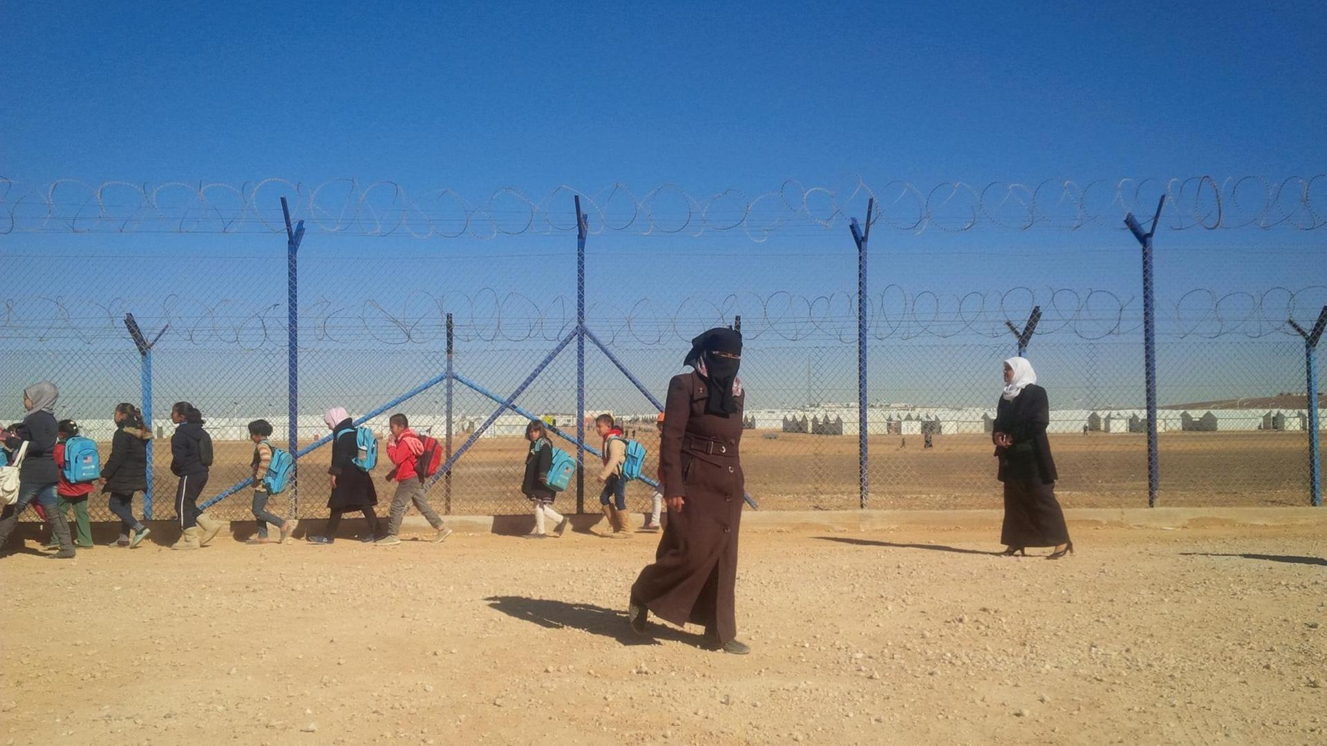 Eine Lehrerin und Schulkinder vor einem Zaun im jordanischen Flüchtlingslager Azraq