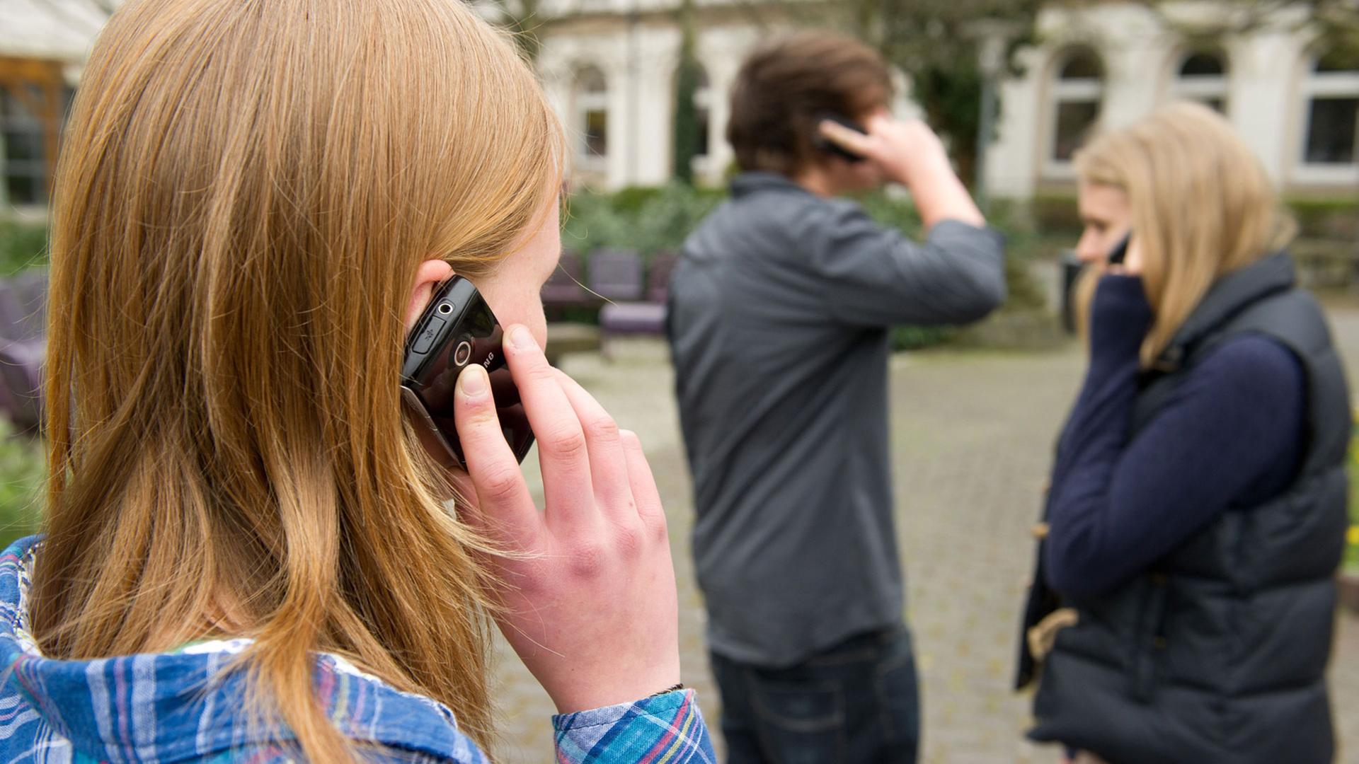 Drei Schüler telefonieren mit ihren Handys auf dem Pausenhof.