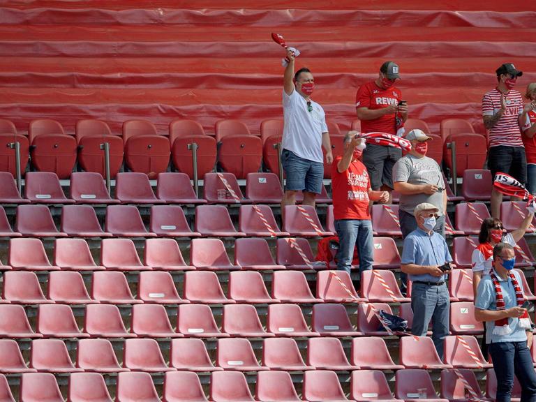 Jubelnde FC Fans mit Mundschutz, auf einer halb leeren Zuschauertribüne in Köln.