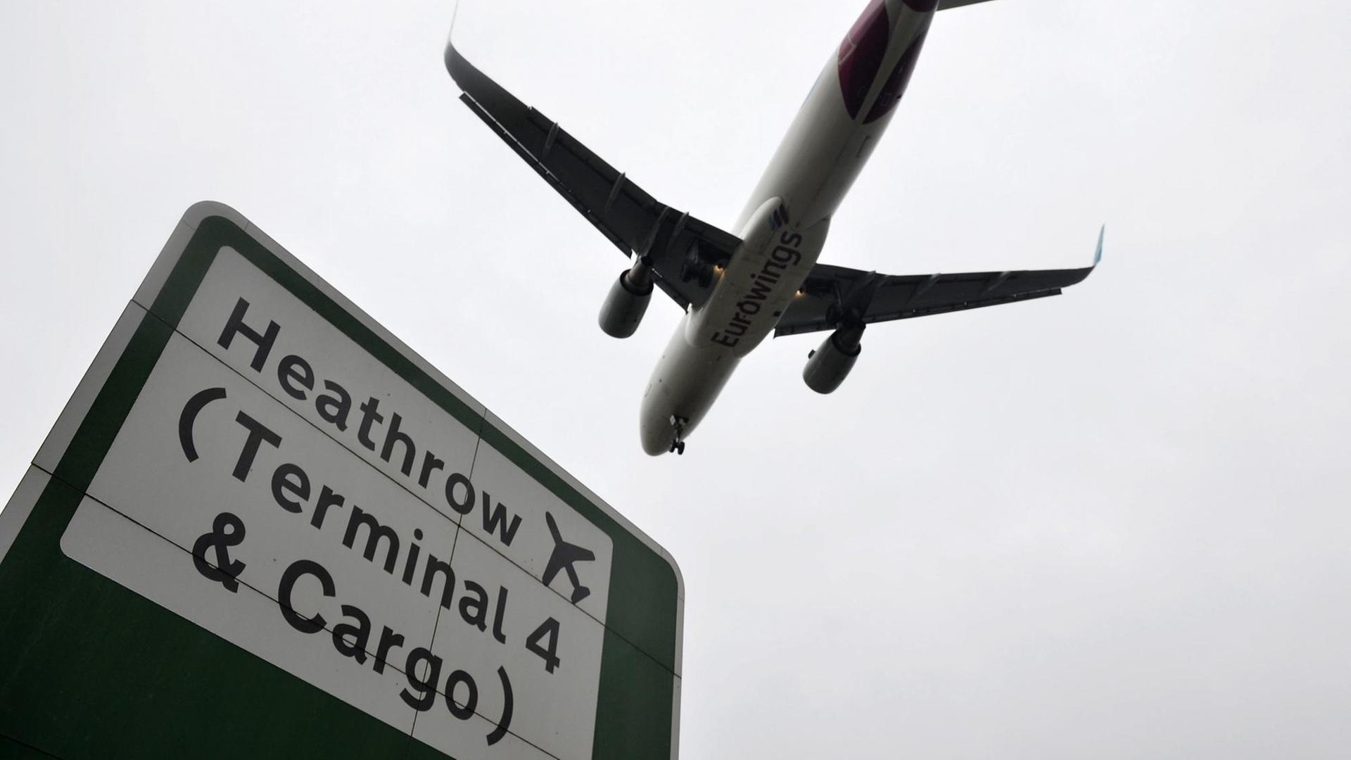 Blick auf ein Flugzeug von unten und einem Schild mit der Aufschrift "Heathrow (Terminal 4 & Cargo)