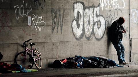 Ein obdachloser Mann steht am 9.8.2016 neben einem Schlafsack und einem Fahrrad unter einer Brücke am Bahnhof Zoo in Berlin.