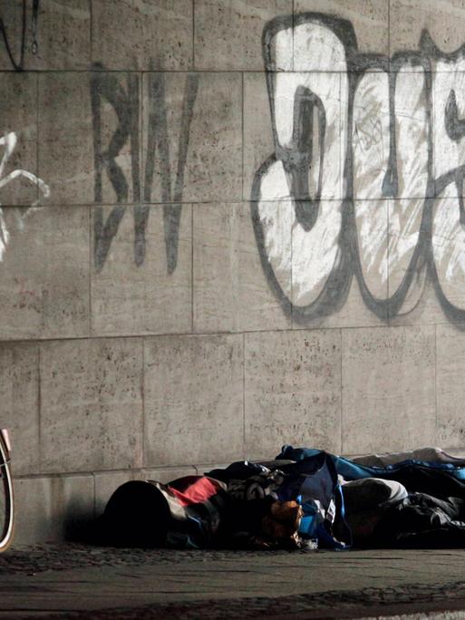 Ein obdachloser Mann steht am 9.8.2016 neben einem Schlafsack und einem Fahrrad unter einer Brücke am Bahnhof Zoo in Berlin.