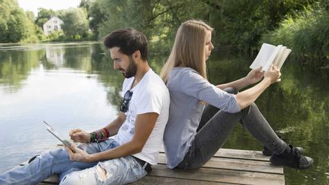 Ein junges Paar sitzt an einem See und liest.
