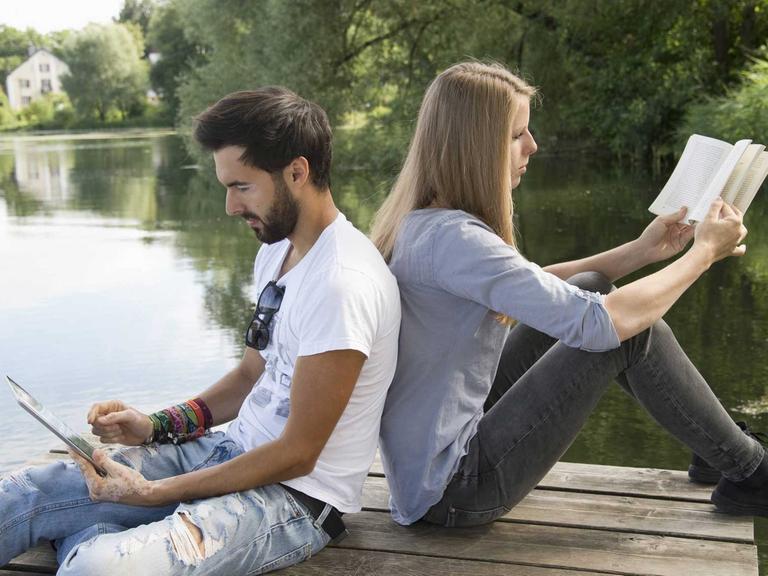 Ein junges Paar sitzt an einem See und liest.