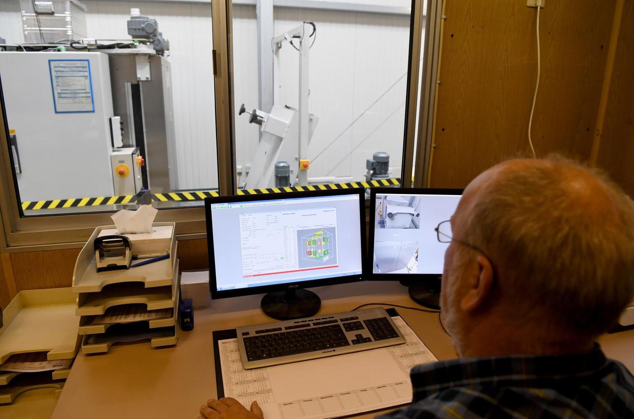 An Mann sitzt vor einem Computer. im Hintergrund sieht man die Maschine, mit der die Radioaktivität des untersuchten Materials ermittelt wird