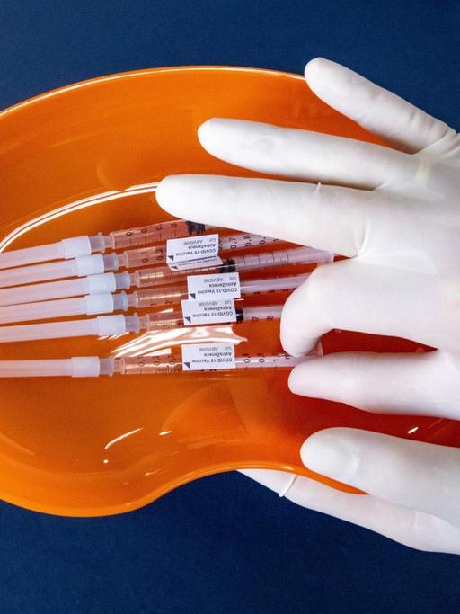 Zwei Hände in Handschuhen halten die ettiketierten Impfdosen 