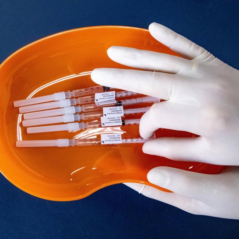 Zwei Hände in Handschuhen halten die ettiketierten Impfdosen, Symolfoto