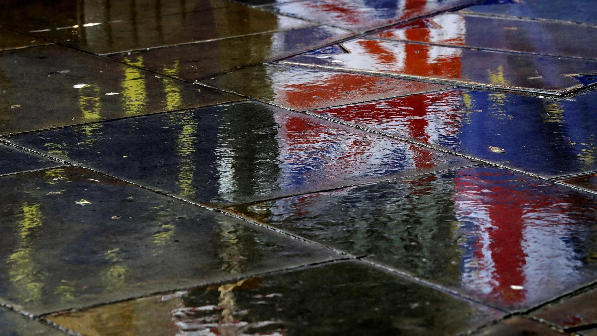 Flaggen spiegeln sich auf dem regennassen Pflaster vor dem britischen Parlament