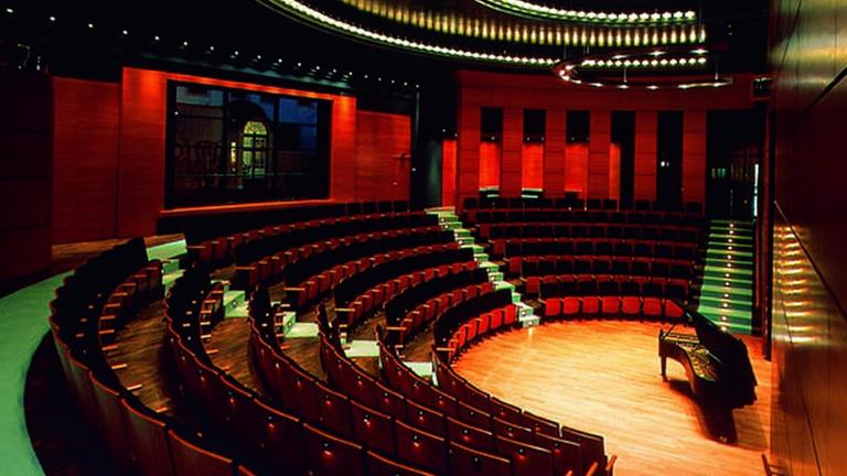 Ein halbrundes Auditorium mit steilen Publikumsreihen um einen halbrunden Bühnenraum, in dem ein Flügel steht.