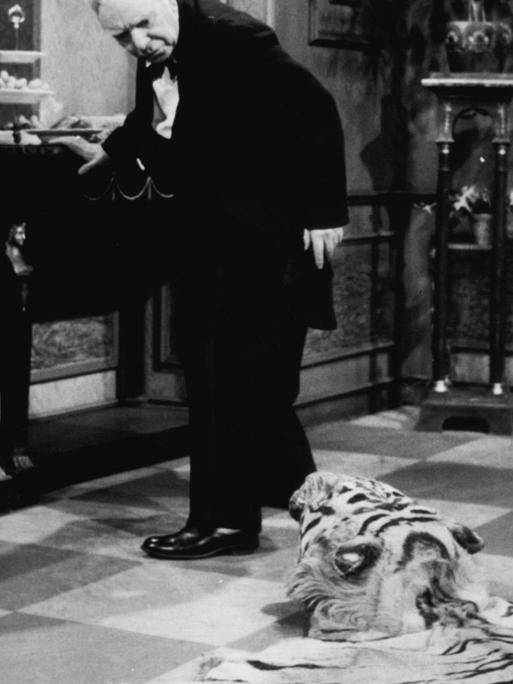 Das Bild zeigt den Butler Freddie Frinton aus dem Sketch "Dinner for one". Er schaut auf das am Boden liegende Tigerfell.