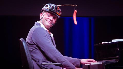 Reinald Grebe mit guter Laune beim Sächsischen Unternehmerpreis im Alten Schlachthof. Auf dem Kopf trägt er einen Fahrradhelm und ein Wiener Würstchen an einer Stange.