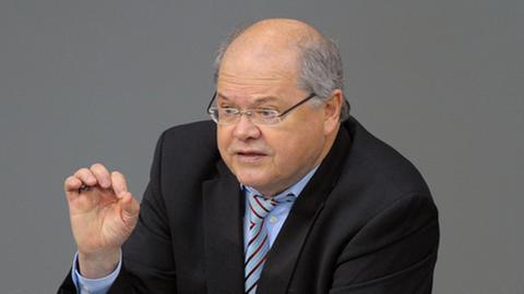 Jerzy Montag, ehemaliger Grünen-Bundestagsabgeordneter, steht an einem Rednerpult und hebt beim Sprechen die rechte Hand. 