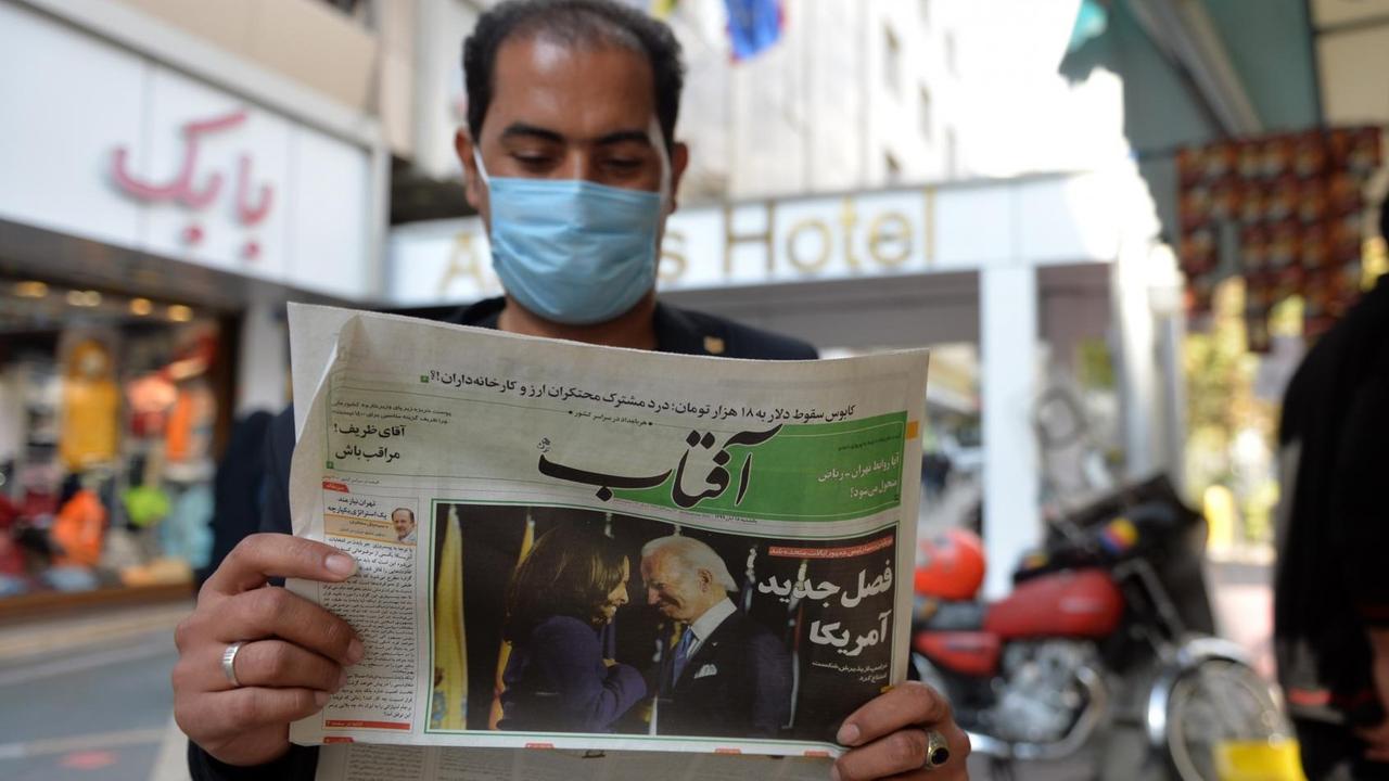 Ein Mann liest auf der Straße in Teheran (Iran) Zeitung. Im Aufmacher zeigt das Blatt den neuen US-Präsidenten Joe Biden.