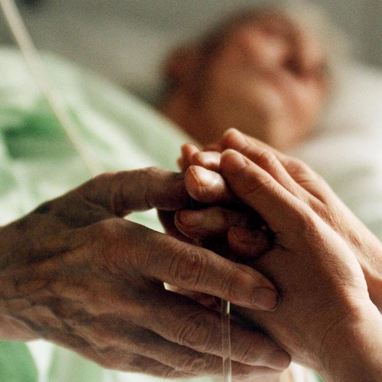 Eine Krankenschwester hält die Hand einer sterbenskranken Patientin