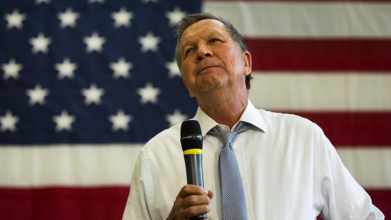 Kasich mit Mokrofon vor einer übergroßen US-Fahne.