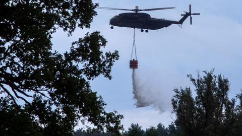 03.07.2019, Mecklenburg-Vorpommern, Jessenitz: Ein Hubschrauber der Bundeswehr wirft Löschwasser über dem brennenden Waldgebiet ab. Die Lage im Waldbrandgebiet auf einem ehemaligen Truppenübungsplatz bei Lübtheen in Mecklenburg-Vorpommern hat sich erstmals seit Ausbruch des Feuers leicht entspannt. Erste Bewohner konnten in ihre vorsorglich geräumten Häuser zurückkehren. Foto: Jens Büttner/dpa-Zentralbild/dpa | Verwendung weltweit