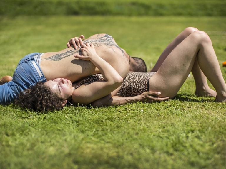 Ein Mann und eine Frau liegen während einer Massage-Workshops ineinander verschlungen auf einer Wiese.