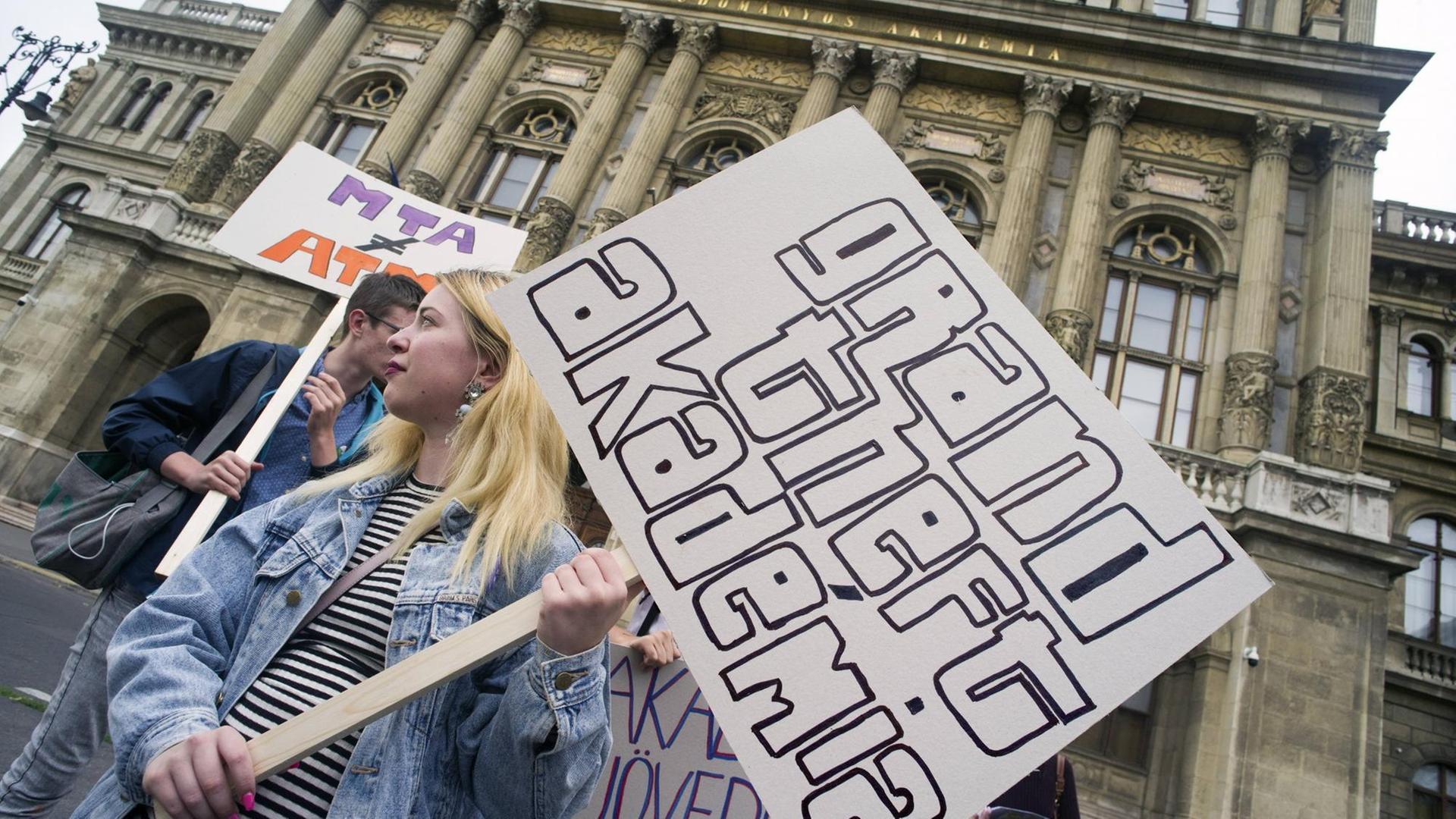 Eine Demonstrantin vor der Akademie der Wissenschaften in Budapest hält ein Schild mit der Aufschrift "Grand Theft Akadémia"