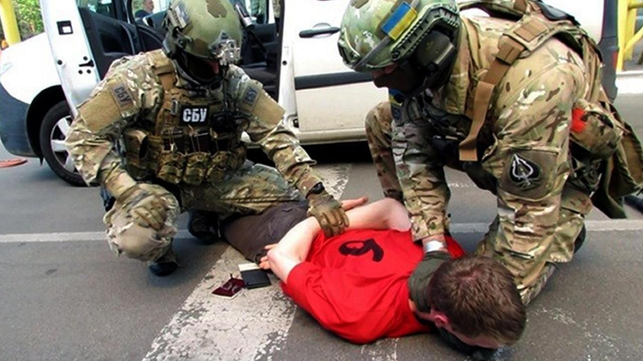 Zwei Polizisten drücken einen Mann auf den Boden und legen ihm Handschellen an.