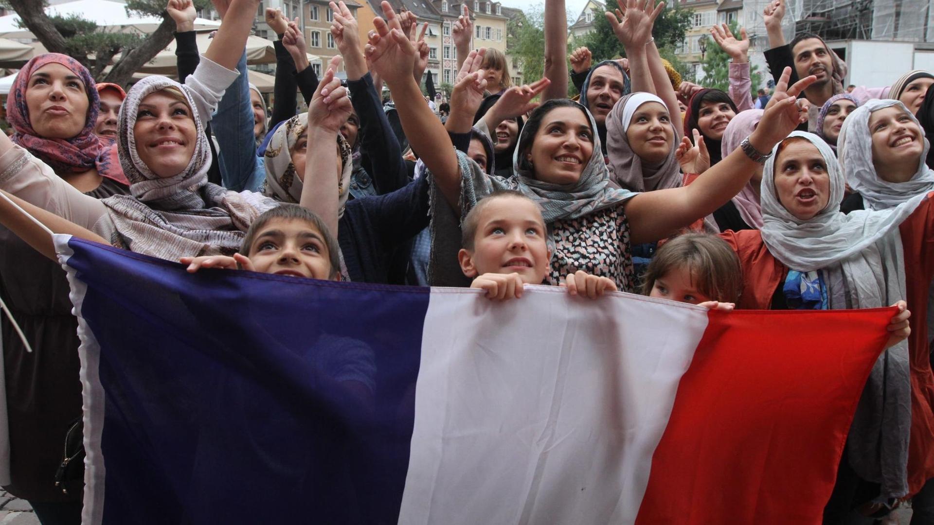 Foto einer Demonstration in Mulhouse gegen die Diskriminierung verschleierter Musliminnen - die Demonstranten halten eine große französische Flagge als Transparent in Händen. Foto: Darek Szuster / dpa